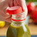 A hand holding a red Unlined Tamper-Evident Cap over a bottle of green juice.