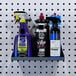 A Triton silver steel shelf with garment hanger holes holding cleaning supplies on a pegboard.