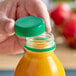 A hand opening a dark green tamper-evident cap on a plastic juice bottle.