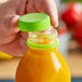 A hand holding a plastic bottle with a lime green tamper-evident cap.