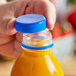 A hand opening a plastic bottle of juice with a royal blue tamper-evident cap.