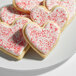 A plate of heart-shaped sugar cookies decorated with white icing and red sanding sugar.