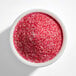 A white bowl filled with fine red and pink sanding sugar.