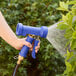 A hand holding a blue Regency front trigger spray nozzle spraying water on plants.