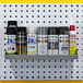 A Triton gray steel shelf holding white and black spray paint cans on a white pegboard.