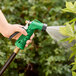 A hand holding a green and black hose spraying water with a Regency green metal garden spray nozzle.