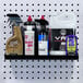 A Triton Products black steel shelf holding cleaning products on a pegboard.