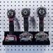 A black shelf holding three Triton Products cordless drills and drill heads.