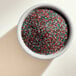 A bowl of colorful Adourne Christmas sanding sugar on a white surface.