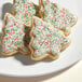 A plate of Christmas tree shaped cookies with white frosting and red and green sprinkles.