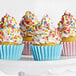 A group of cupcakes with white frosting and colorful rainbow sprinkles in blue and pink wrappers.