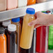 A person holding a 12 oz. round PET clear juice bottle with a royal blue lid.