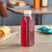 A 16 oz. Square Milkman PET clear juice bottle with red liquid and a white lid on a table.