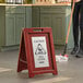 A woman using a Lavex Wood A-Frame wet floor sign to clean a floor.