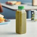 A 16 oz. tall square rPET clear juice bottle with green liquid on a table.