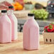 A close-up of a pink 32 oz. Square Milkman PET juice bottle with a black lid.