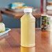 A close up of a 15.2 oz. square PET clear juice bottle with yellow liquid inside on a table.