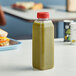 A 16 oz. tall square clear rPET juice bottle with green liquid and a red cap on a table.