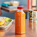 A 14.5 oz. square PET clear juice bottle with a red lid on a table next to a sandwich.