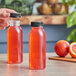 Two people pouring orange juice into 8 oz. round PET clear juice bottles with black lids on a counter.