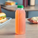 A close-up of a 16 oz. clear square juice bottle filled with pink liquid and closed with a green cap.