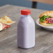 A 12 oz. clear square PET juice bottle with red liquid and a red cap on a table.