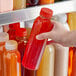 A hand holding a 16 oz. clear plastic juice bottle with red liquid inside.