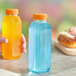 A hand holding a 10 oz. square PET clear juice bottle with yellow liquid.