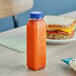 A 12 oz. clear rPET juice bottle with a blue lid on a table next to a sandwich.