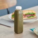 A sandwich and a bottle of green liquid on a table with a 12 oz. tall square rPET clear juice bottle and clear lid.