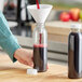 A person pouring red liquid into a 12 oz. clear juice bottle.
