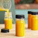A group of 2.5 oz. yellow PET round bottles with black lids filled with orange liquid.