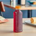 A 16 oz. square PET clear juice bottle with red liquid and an orange lid on a table.