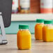 Square PET clear energy bottles with green lids filled with orange juice on a counter.