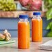 Two 8 oz. round PET clear juice bottles with blue lids filled with orange juice on a counter.