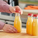 A person pouring orange juice into a 12 oz. round PET clear carafe juice bottle.