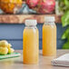 Two 8 oz. round PET clear juice bottles with clear lids on a table.