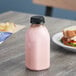 A square clear rPET juice bottle with a black lid filled with pink liquid next to a sandwich.