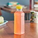 A 15.2 oz. square PET clear juice bottle with a yellow lid on a table.