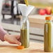 A person pouring green juice into a Round PET Clear Juice Bottle.