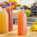 A person holding a 32 oz. clear Juice Bottle of yellow liquid next to a lemon.