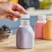 A hand holding a square clear PET juice bottle filled with purple liquid.