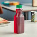 A 16 oz. square PET clear carafe juice bottle with a green lid filled with red liquid on a table.