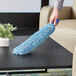 A hand holding a blue Lavex Chenille microfiber duster sleeve over a black surface.