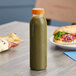 A 12 oz. round clear juice bottle filled with green liquid on a table.