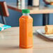 A 16 oz. square PET clear juice bottle with a green lid on a table with a plate of food.