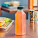 A 14.5 oz. Square PET clear juice bottle on a table with a sandwich.