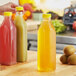 A hand holding a yellow plastic Tall Square Milkman juice bottle.