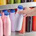 A hand holding a 16 oz. clear plastic juice bottle with a blue lid.