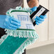 A person in blue gloves holding a black and white rectangular Lavex Microfiber mop pad.